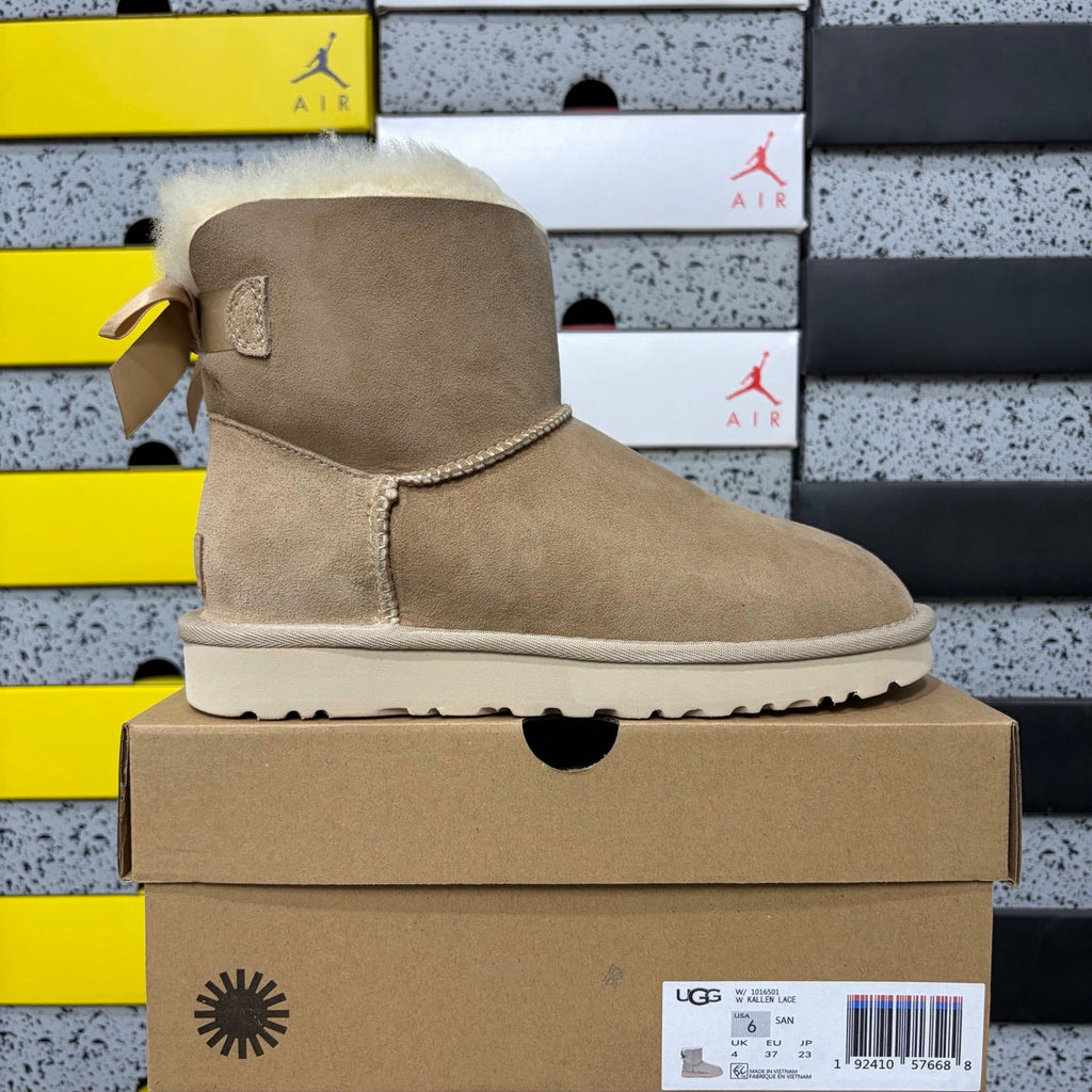 UGG Mini Bailey Bow Ankle Boot – Suede Boot with Cream Shearling Lining, Satin Bow Detail & Sand Sugar Sole in Sand